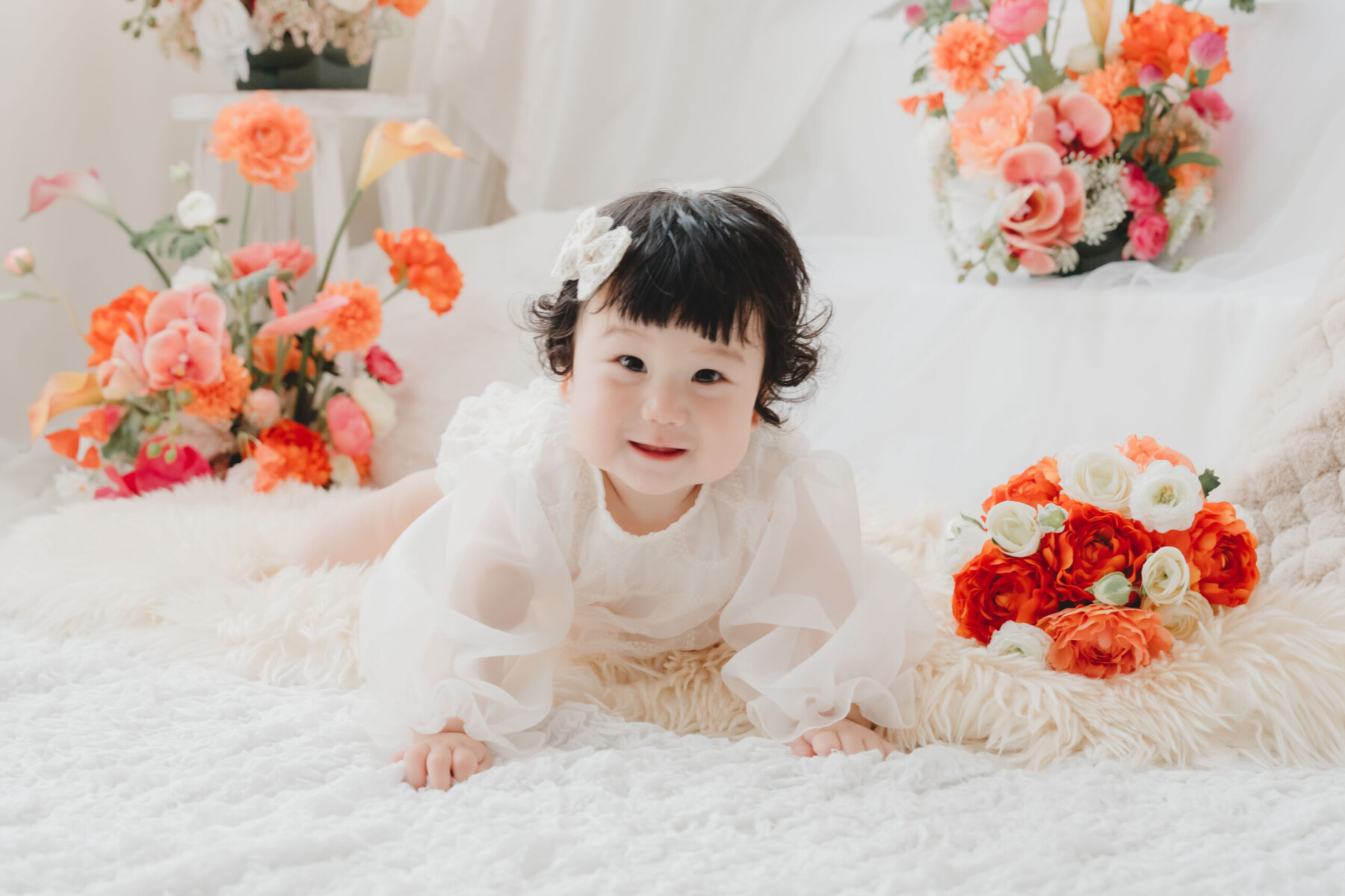 オレンジとピンクの花々に囲まれて撮影した赤ちゃんの成長記念フォト